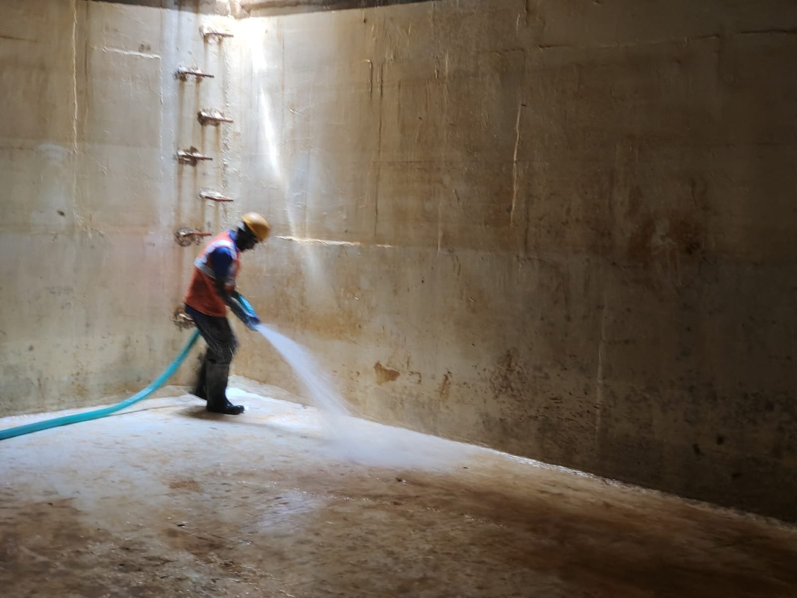 Technician pressure-washing the inside of a large concrete water tank
