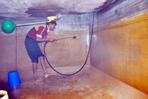 Technician pressure-washing stained water tank walls